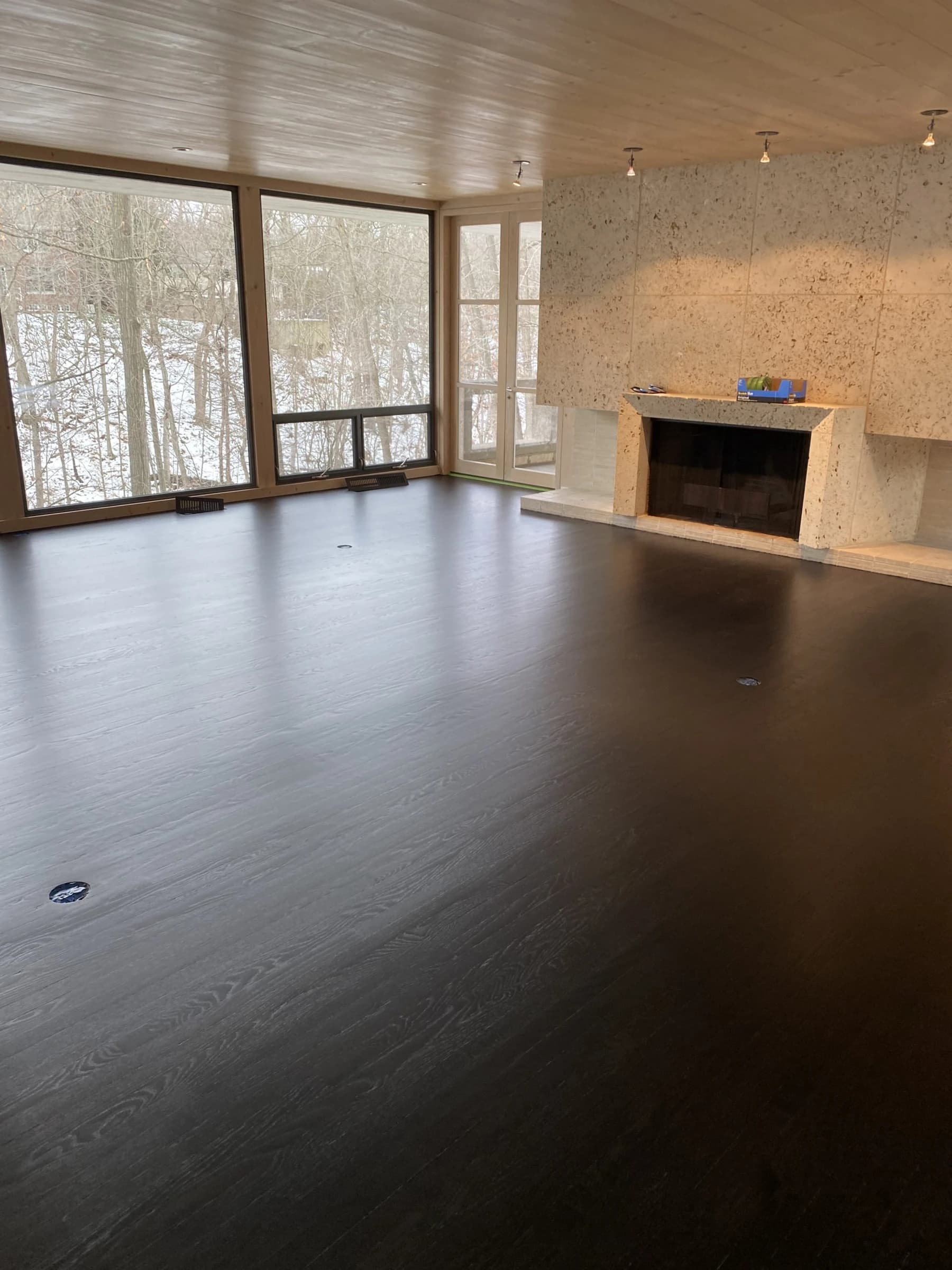 Dark flooring in a room with a stone fireplace and tall windows.